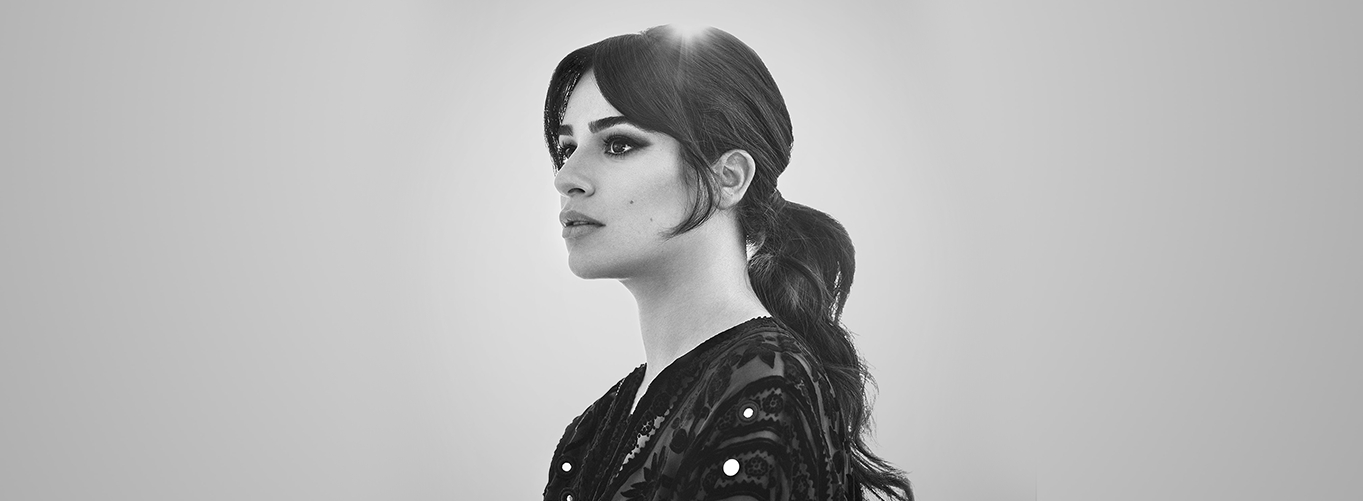 Headshot photo of Lea Michele looking off camera, framing her head from above is the sun glistening into the camera